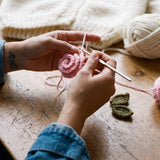Hands crocheting a pink rose for the Rose Cream cardigan in the atelier — handmade by Ana Chic