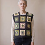 Green granny square crochet vest worn over a beige long-sleeve top