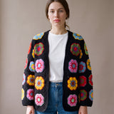 Woman wearing the black crochet cardigan with multicoloured African-flower blocks open over a white tee and jeans - handmade by Ana Chic
