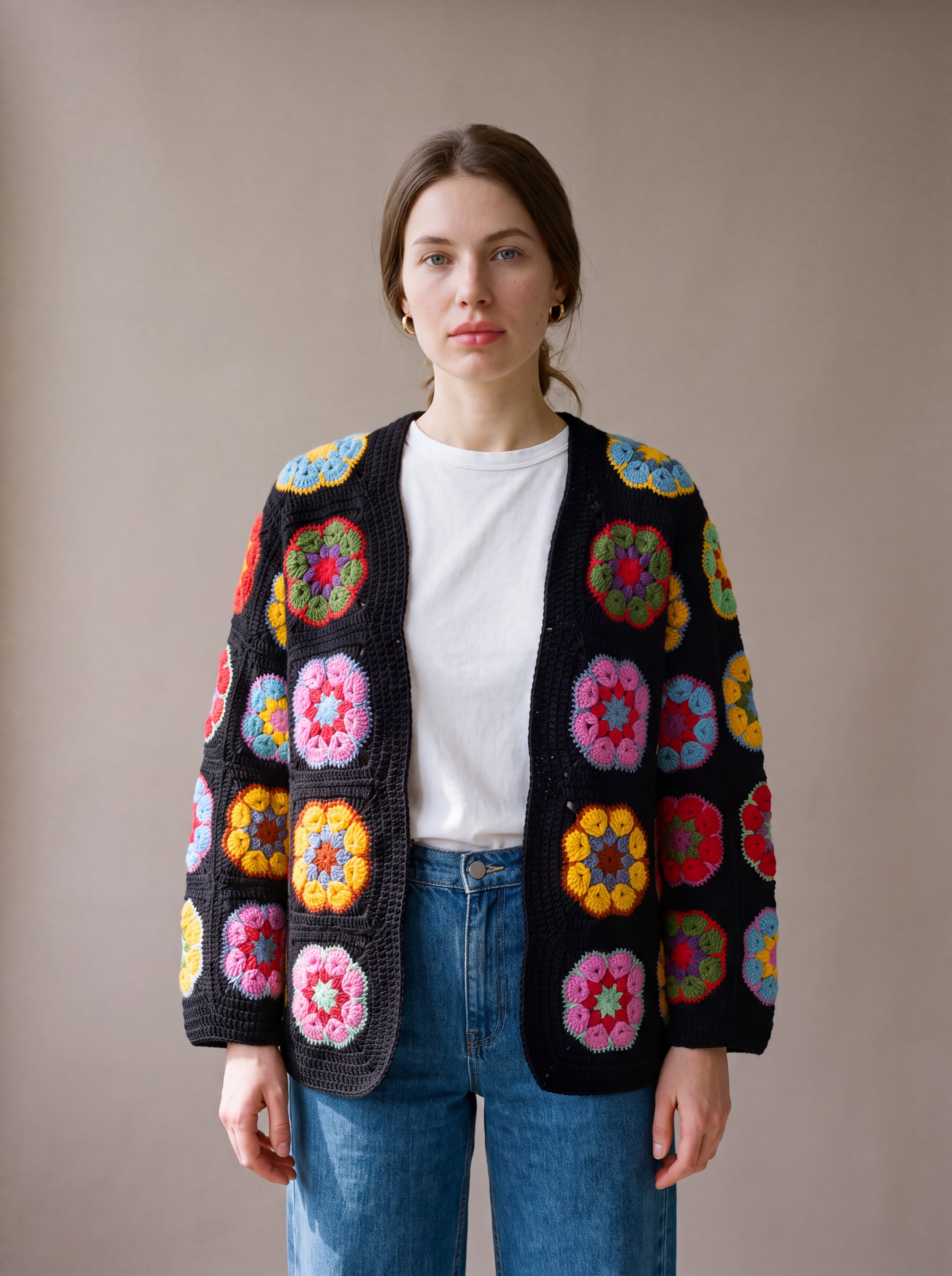 Woman wearing the black crochet cardigan with multicoloured African-flower blocks open over a white tee and jeans - handmade by Ana Chic