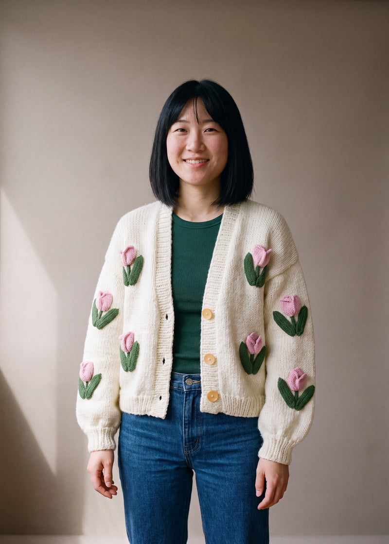 Cream hand-knitted cardigan with pink tulips, worn open over a green top and jeans — handmade by Ana Chic