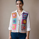 Woman wearing the Confetti Vest, a handmade granny square crochet vest, over a white shirt and dark jeans