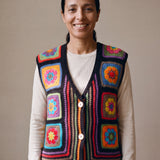 Woman wearing the Electra Vest, a handmade granny square crochet vest, over an oatmeal knit top and dark jeans