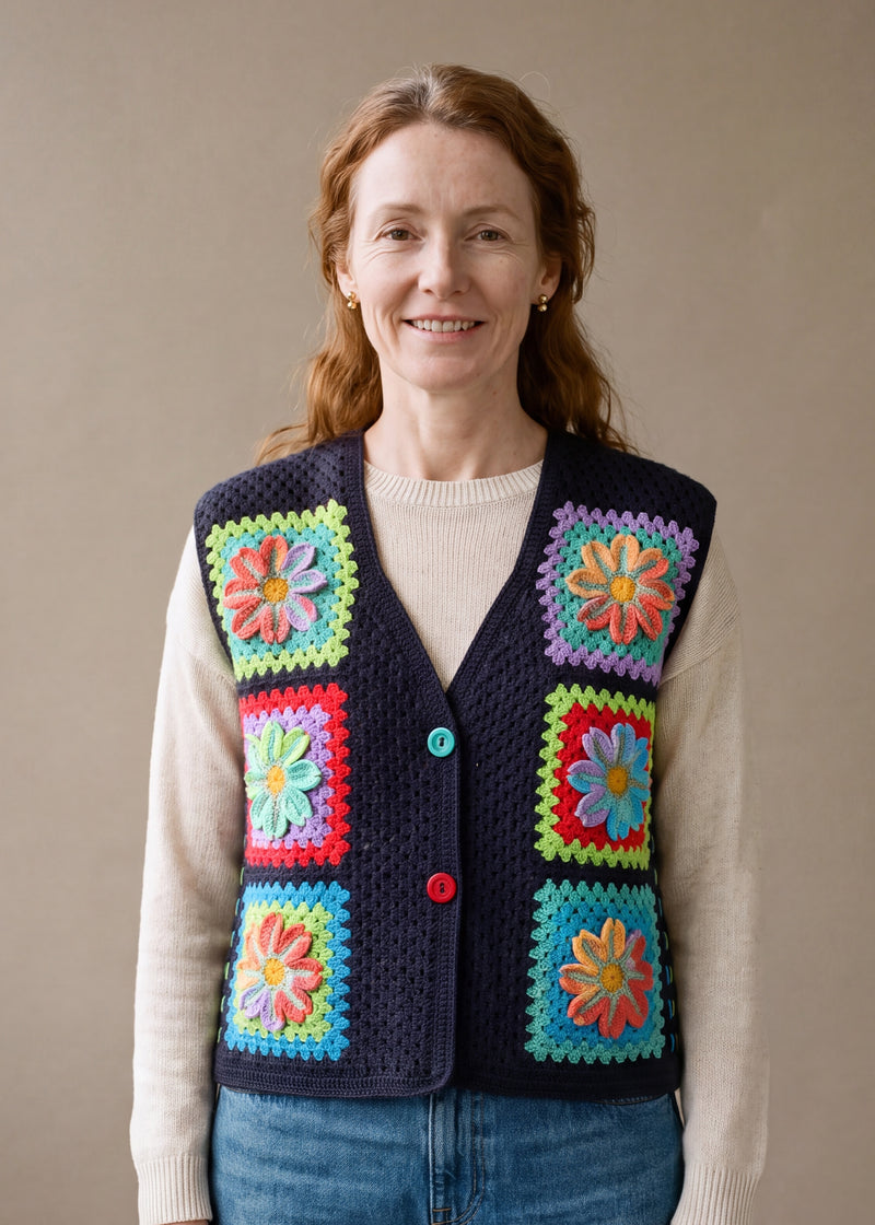 Woman wearing the Moonflower Vest, a handmade granny square crochet vest, over an ecru knit top and blue jeans